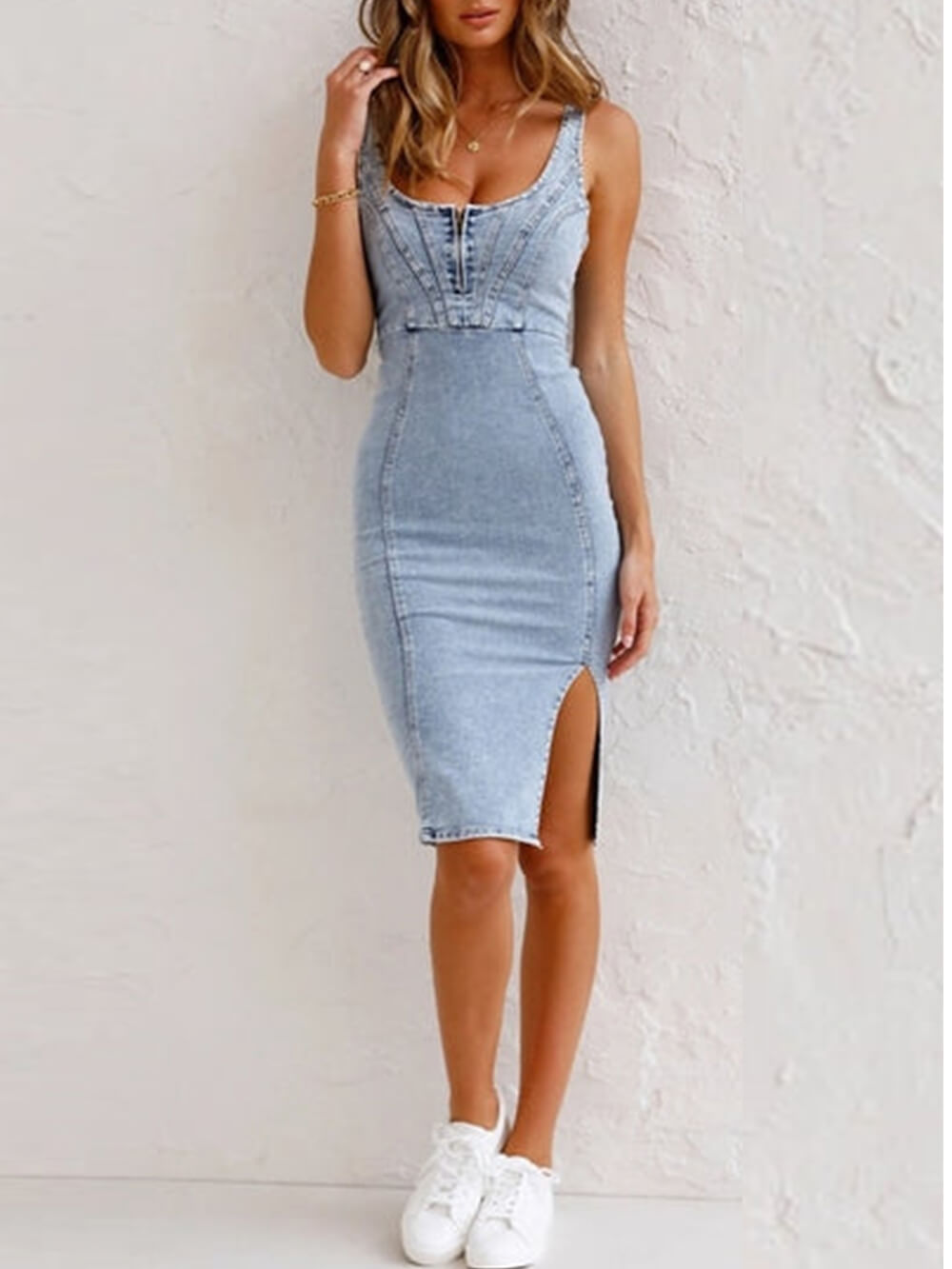 Woman wearing a light blue denim sleeveless sheath dress with a scoop neck, zipper closure, and high slit, posing with hand on head.