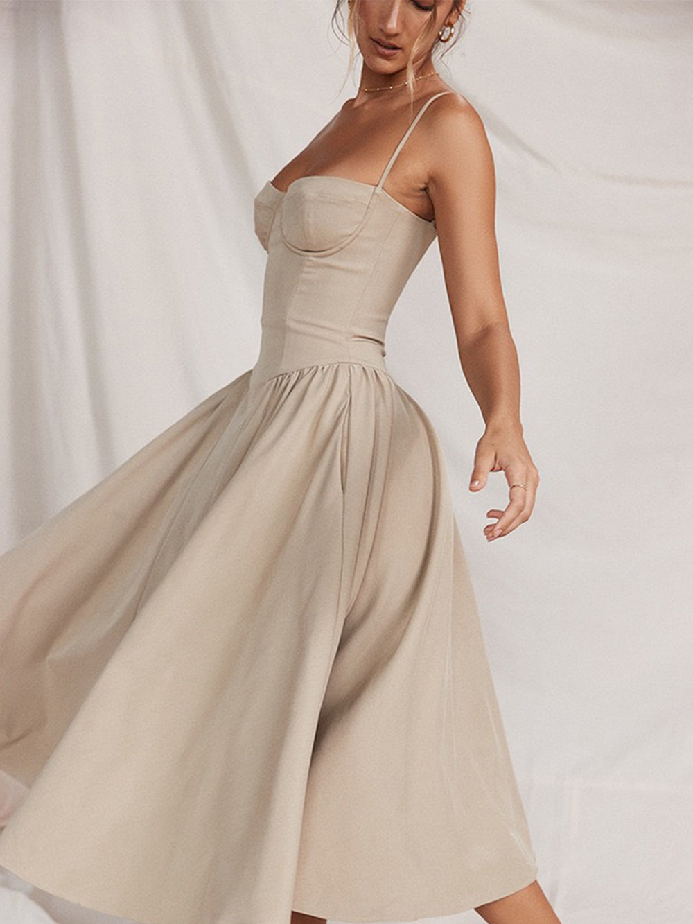 A woman in a beige midi dress with a flowing skirt, captured in a dynamic pose as she twirls.
