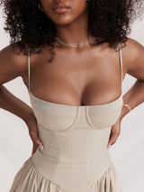 Close-up of a woman wearing a beige midi dress with a sweetheart neckline and spaghetti straps, her hands on her hips.