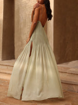 back view of a woman in a pale green pleated maxi dress with thin straps and a high slit, showing her back