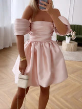 woman in a pink off-the-shoulder mini dress with puffy sleeves and a bubble skirt, holding a white clutch