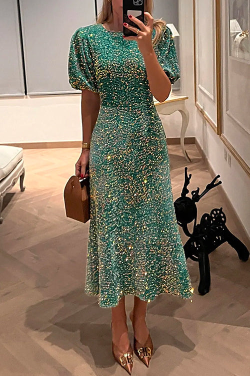 A woman wearing a green sequined midi dress with puff sleeves, holding a brown structured purse and wearing pointed-toe heels.
