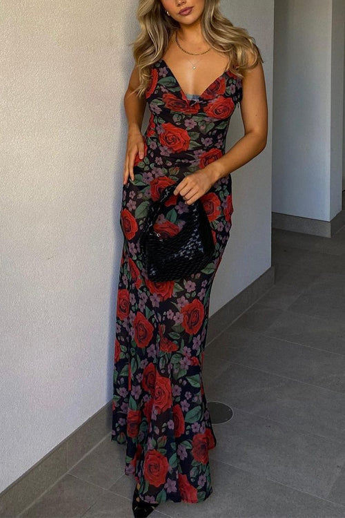 Woman posing in a floral print maxi dress with a black handbag and stiletto heels.