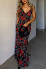 Woman posing in a floral print maxi dress with a black handbag and stiletto heels.