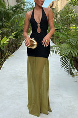 Woman wearing a black halter neck dress with a keyhole cutout and gold hardware detail, paired with a floor-length olive green sheer skirt overlay and carrying a gold clutch, standing on a pathway surrounded by lush greenery.