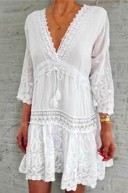 A woman modeling a white bohemian-style dress with lace trim and paisley print.