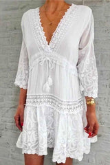 A woman modeling a white bohemian-style dress with lace trim and paisley print.