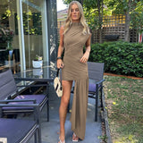A woman in a taupe ruched dress with an asymmetrical hemline stands outdoors.