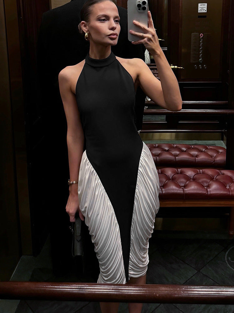 A woman in a black and white halter neck dress with ruched white fabric on the skirt, taking a mirror selfie in an elevator.
