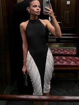 A woman in a black and white halter neck dress with ruched white fabric on the skirt, taking a mirror selfie in an elevator.