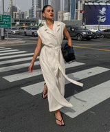 A woman in a long, ivory linen dress walks across a crosswalk in a city.