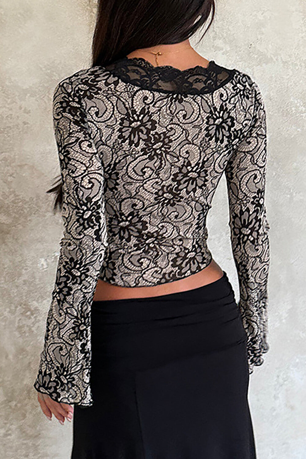 Back view of a woman wearing a black and beige lace long-sleeved top with a plunging neckline and a black skirt