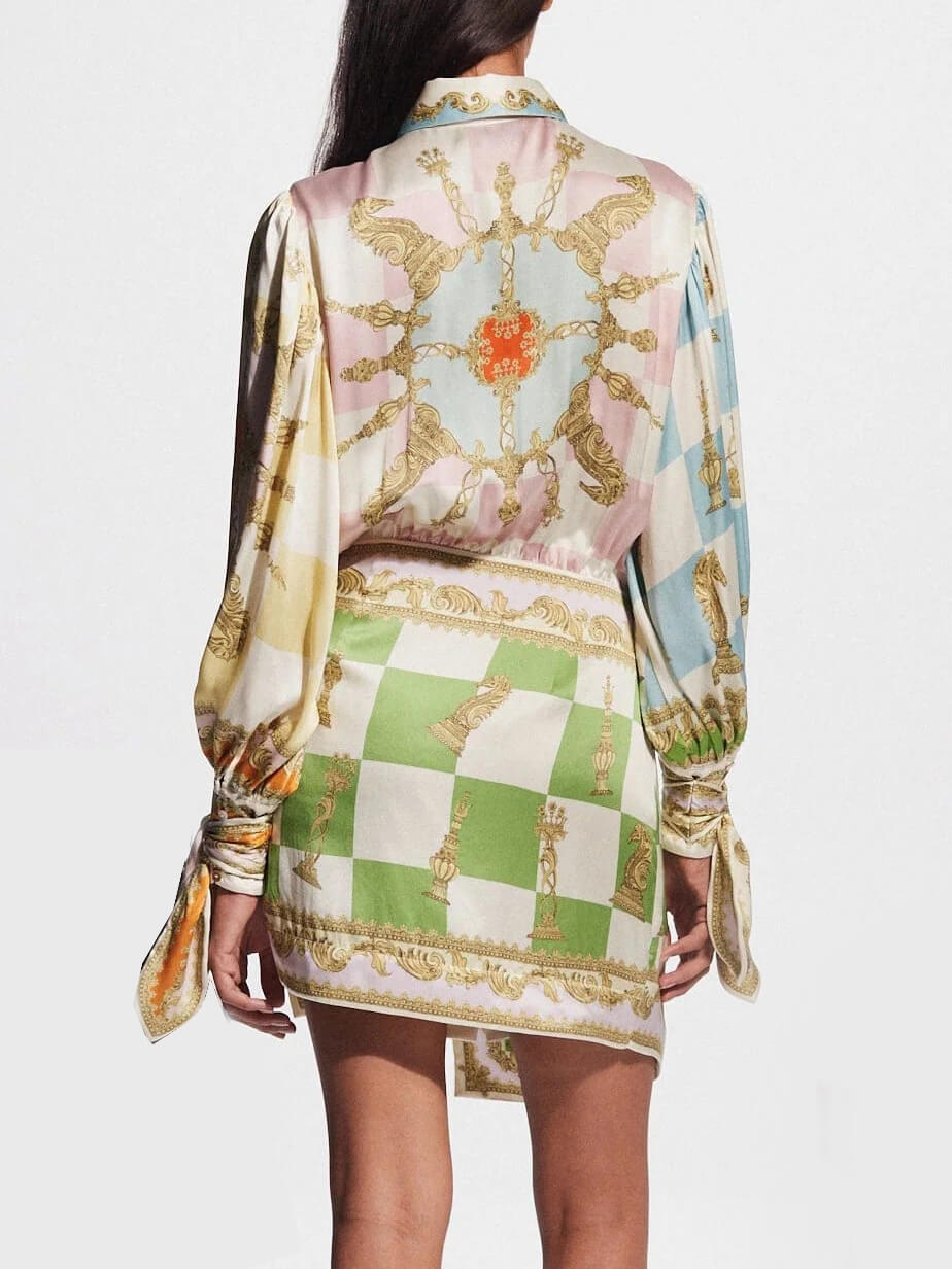 back view of a woman wearing a white, green, orange, blue, pink, and yellow patterned silk shirt dress with a tie waist and puffed sleeves