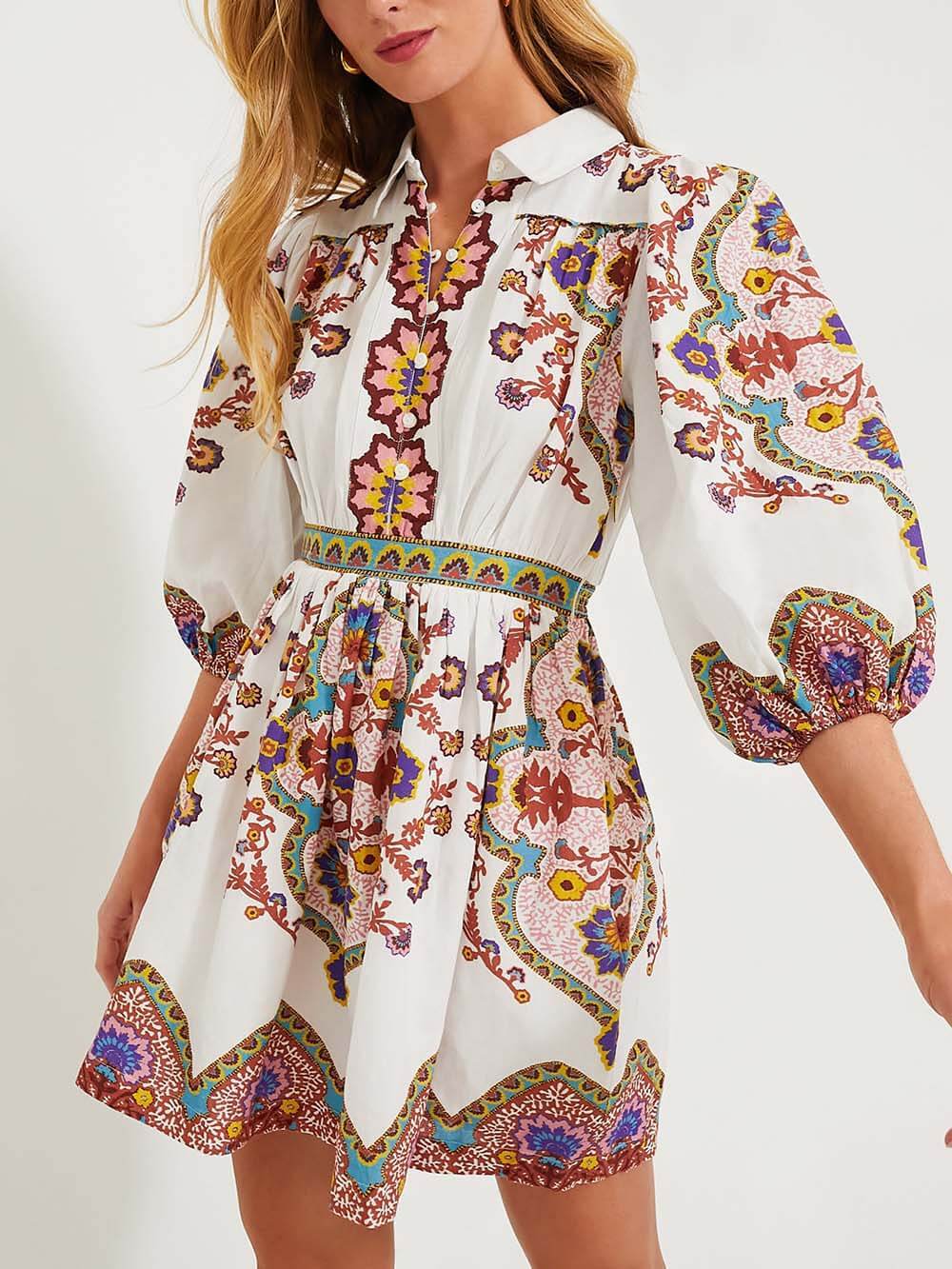 A woman wearing a white short dress with a colorful paisley print and puff sleeves.