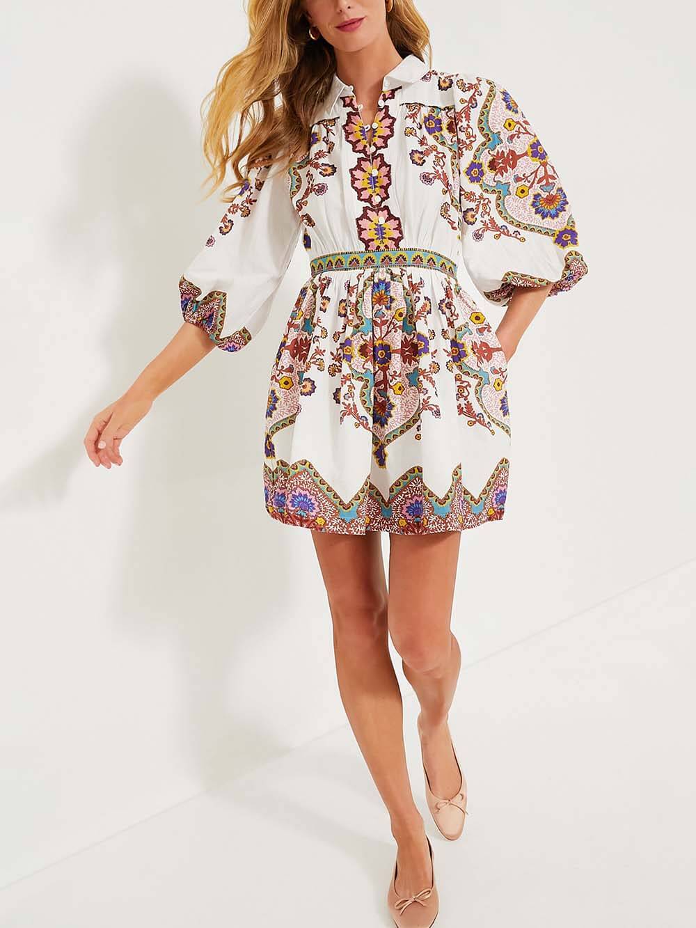 A woman in a white dress with a vibrant paisley print, with her hand on her hip and looking to the side.