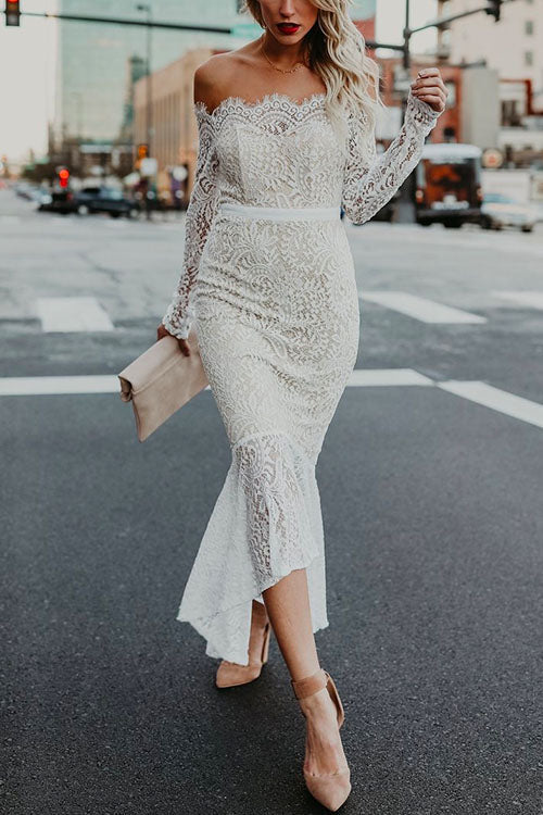 Woman wearing a white off-the-shoulder lace mermaid dress with long sleeves, holding a clutch.