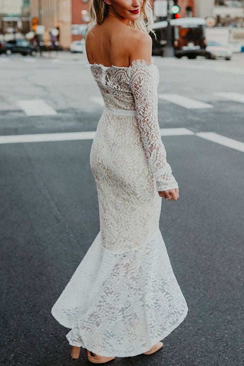 Woman wearing a white off-the-shoulder lace mermaid dress with long sleeves, viewed from the back.