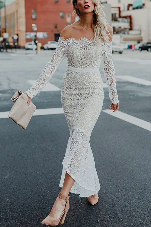 Woman wearing a white off-the-shoulder lace mermaid dress with long sleeves, walking across a street.
