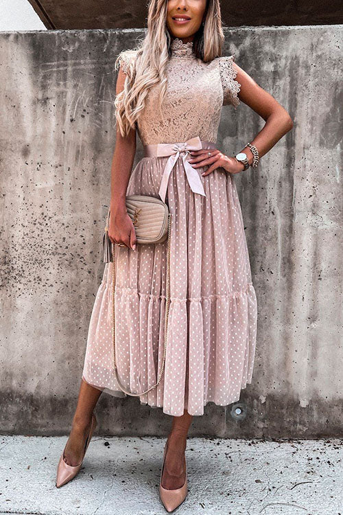 Woman wearing a pink polka dot midi dress with a lace top and a bow belt.