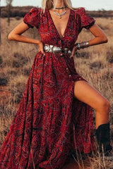 Woman posing in a red paisley maxi dress with a high slit, silver belt, and cowboy boots in a dry field, showing the front of the dress.