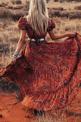 Rear view of a woman in a flowing red paisley maxi dress with a wide silver belt, her skirt billowing around her.