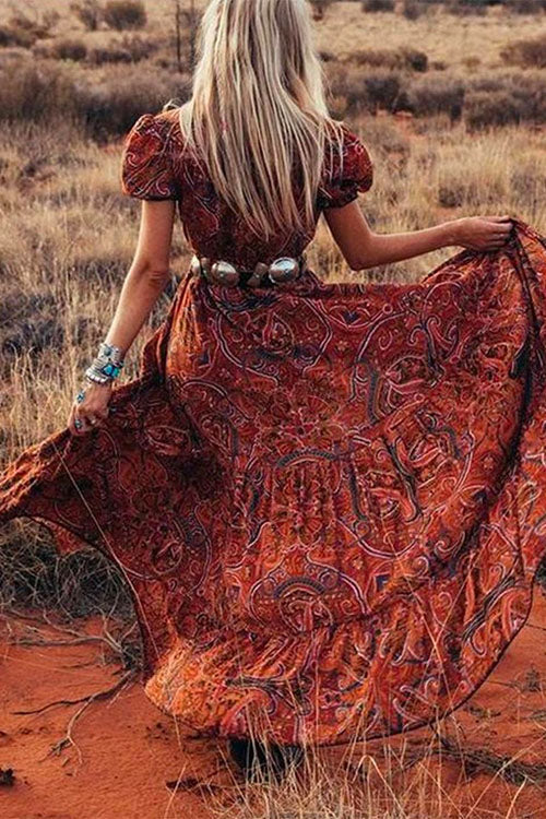 Rear view of a woman in a flowing red paisley maxi dress with a wide silver belt, her skirt billowing around her.