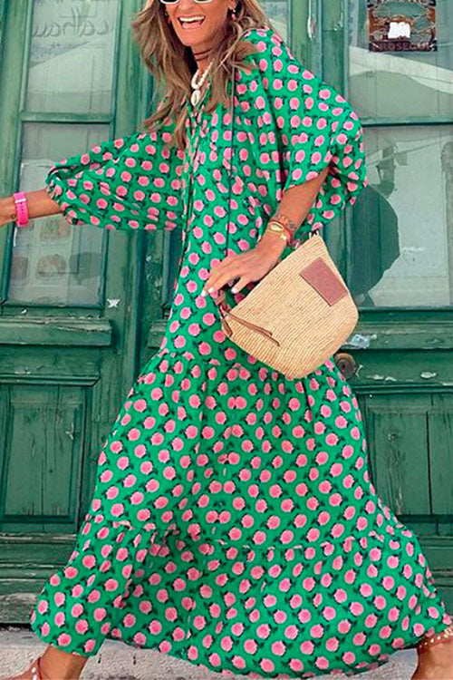 Woman in a flowing green floral print dress walking, with a straw bag and sandals.