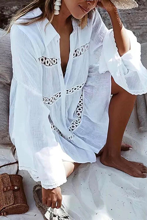 Woman wearing a white sheer dress with black embroidered details and ruffled sleeves, sitting on a beach.