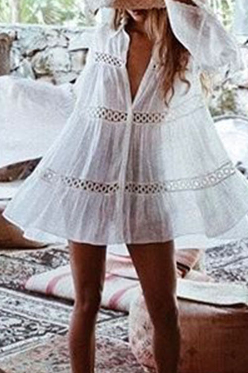 Woman wearing a white sheer dress with black embroidered details and ruffled sleeves, standing indoors.