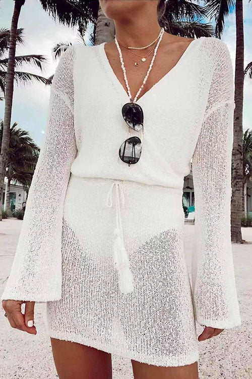 Close-up of a woman wearing a white knit mini dress with a wrap front and bell sleeves, accessorized with sunglasses and necklaces.