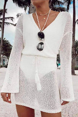 Close-up of a woman wearing a white knit mini dress with a wrap front and bell sleeves, accessorized with sunglasses and necklaces.