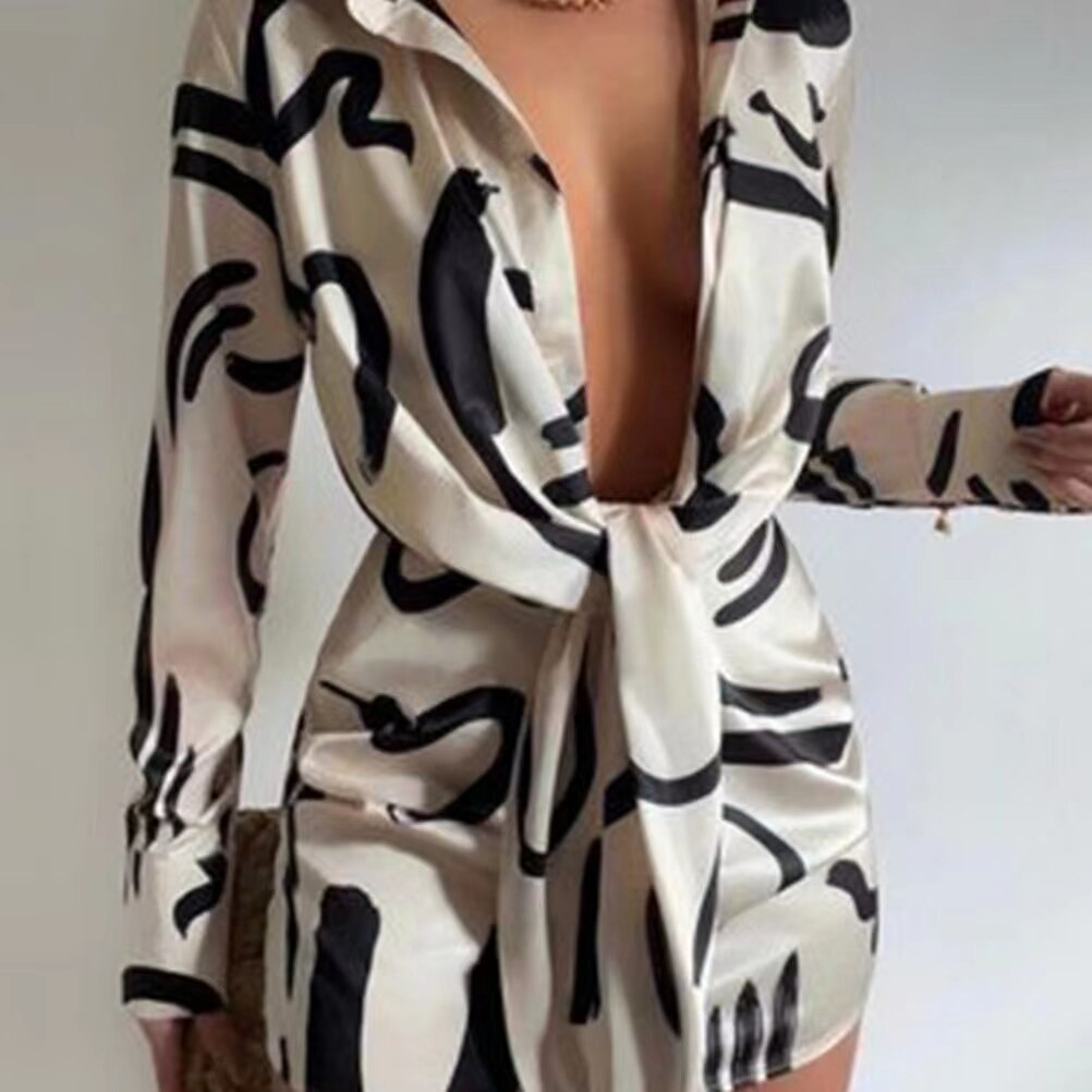 A woman in a long-sleeved beige dress with a black abstract print and a tie-front detail.