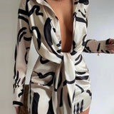 A woman in a long-sleeved beige dress with a black abstract print and a tie-front detail.