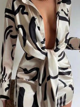 Close-up of a woman's chest and shoulders in a beige shirt dress with a black abstract print and a tie-front.