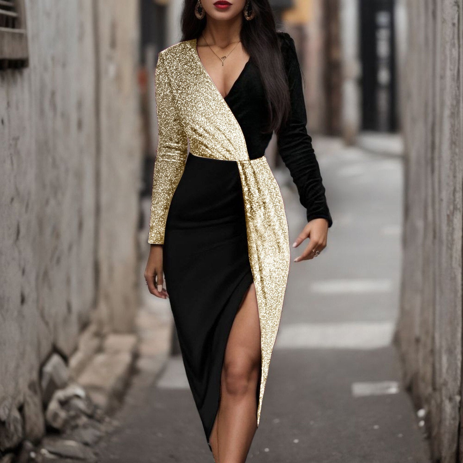 Woman wearing a black and gold sequined wrap dress with a high slit, standing in an alley.
