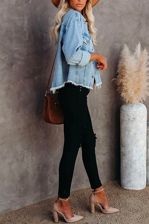Side view of a woman in a light blue distressed denim jacket, white tank top, black ripped jeans, brown belt, and nude heels, with a tan hat and brown crossbody bag.