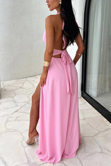 Back view of a woman in a pink halter maxi dress with a tie-back detail and a high slit.