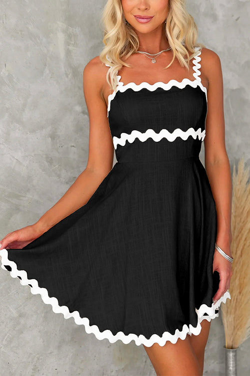 Front view of a woman wearing a black fit and flare mini dress with white scalloped trim on the straps and hem.