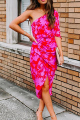 full body shot of a woman in a pink and red floral one-shoulder sheath dress, paired with beige heels and a clutch