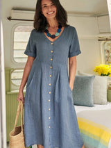 Woman wearing a blue button-down midi dress with short sleeves and pockets, holding a straw bag.