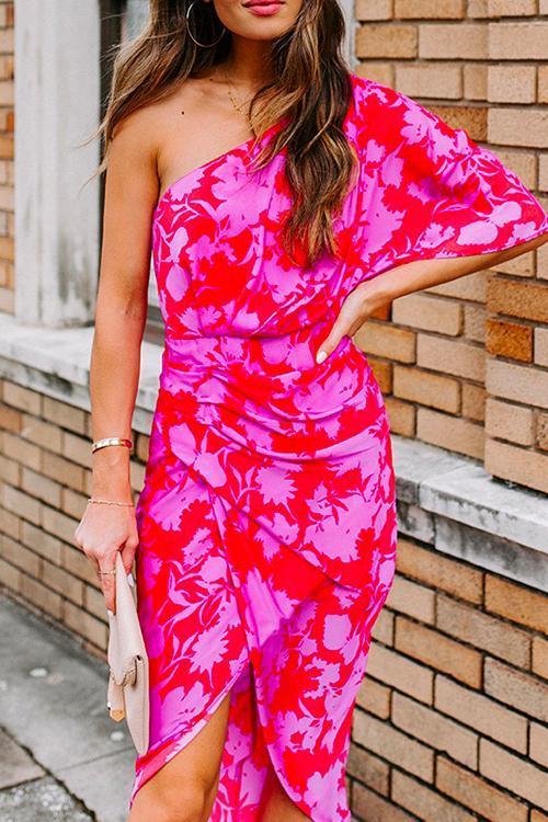 woman wearing a pink and red floral one-shoulder sheath dress with a ruched waist and tulip hem, holding a beige clutch