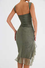 Back view of a woman in an olive green ruched mesh dress, showing the zipper closure and ruffled hem.