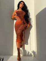 A woman leaning against a wall in a brown and orange abstract print one-shoulder midi dress.