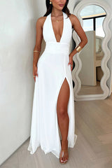 A woman in a white halter maxi dress with a deep V-neck and a thigh-high slit.