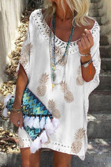 woman wearing a white pineapple print kaftan dress with lace trim, layered necklaces, and a colorful tasseled clutch
