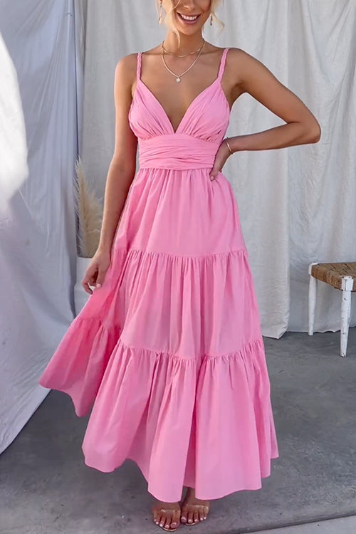 A woman in a pink tiered maxi dress with spaghetti straps and a ruched bodice, standing outdoors.