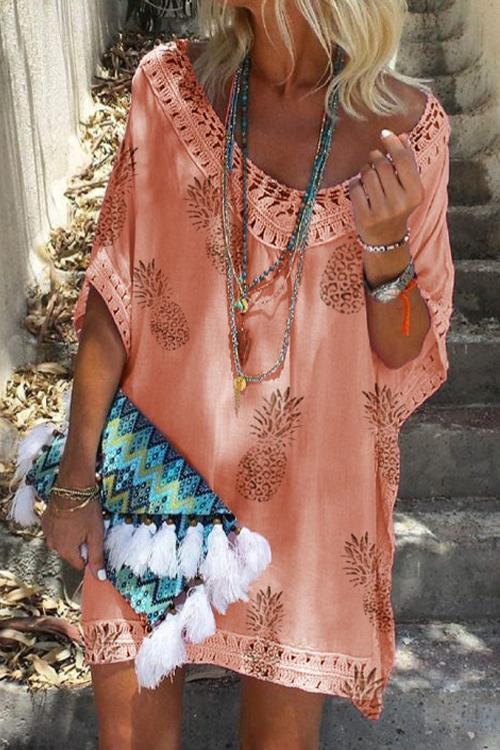 woman wearing a peach pineapple print kaftan dress with lace trim, layered necklaces, and a colorful tasseled clutch