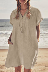 Woman wearing a tan linen-like short-sleeved collared shirt dress with pockets and a necklace, standing on a beach.