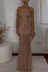 Woman in a floor-length, sequined beige dress with spaghetti straps, holding a gold clutch.