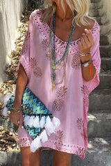 woman wearing a pink pineapple print kaftan dress with lace trim, layered necklaces, and a colorful tasseled clutch